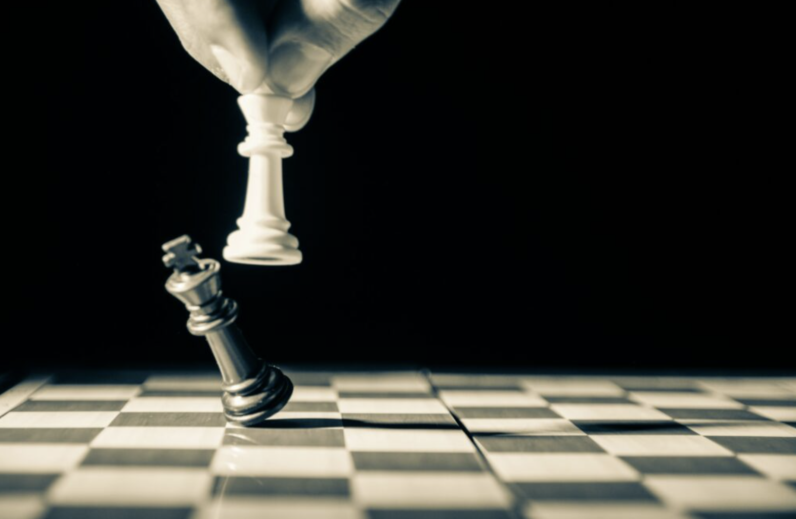 A white queen toppling a black king on a chessboard, symbolising checkmate